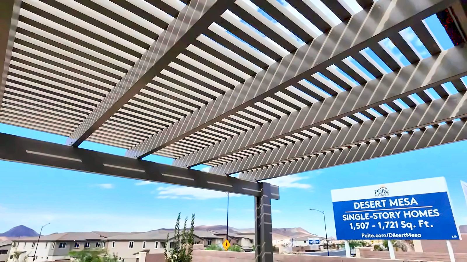 Covered pergola at the Desert Mesa model complex with a Desert Mesa single-story homes sign and mountains in the background