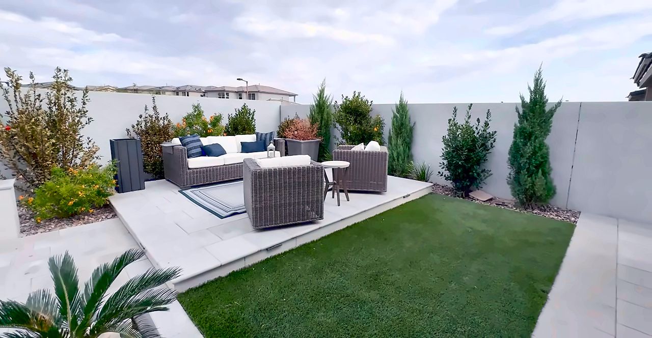 Backyard with artificial turf, a covered patio, outdoor sofas and cypress trees behind a Summerlin home