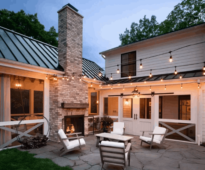An inviting stone patio with a brick outdoor fireplace and string lights designed for summer evenings in Harrisonburg.