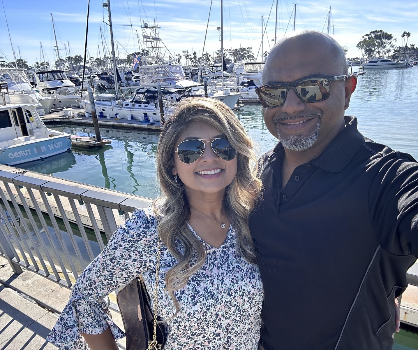 Jasmine Sayeed, REALTOR®, and her husband at Dana Point Harbor with boats in the marina behind her