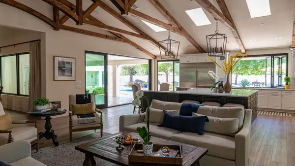 Open-plan luxury living room with wood beam ceilings and glass doors opening to a pool patio