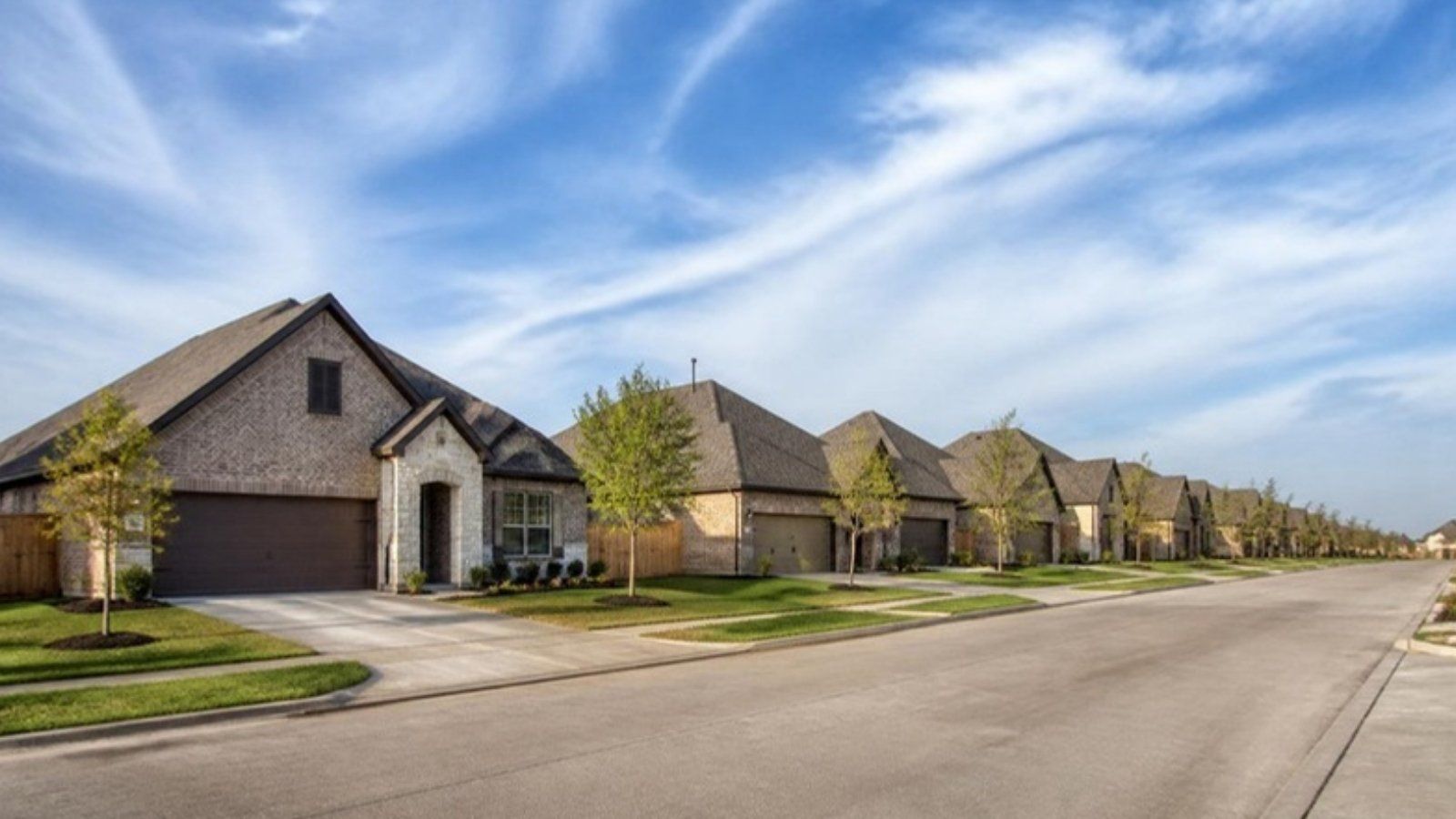 Row of newly built brick homes on a curved street in a master-planned community near Brookshire, TX