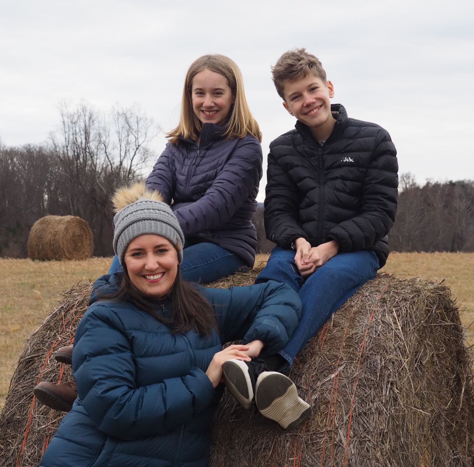 Dory with kids sitting on a hay bale with the Charlottesville mountains in background