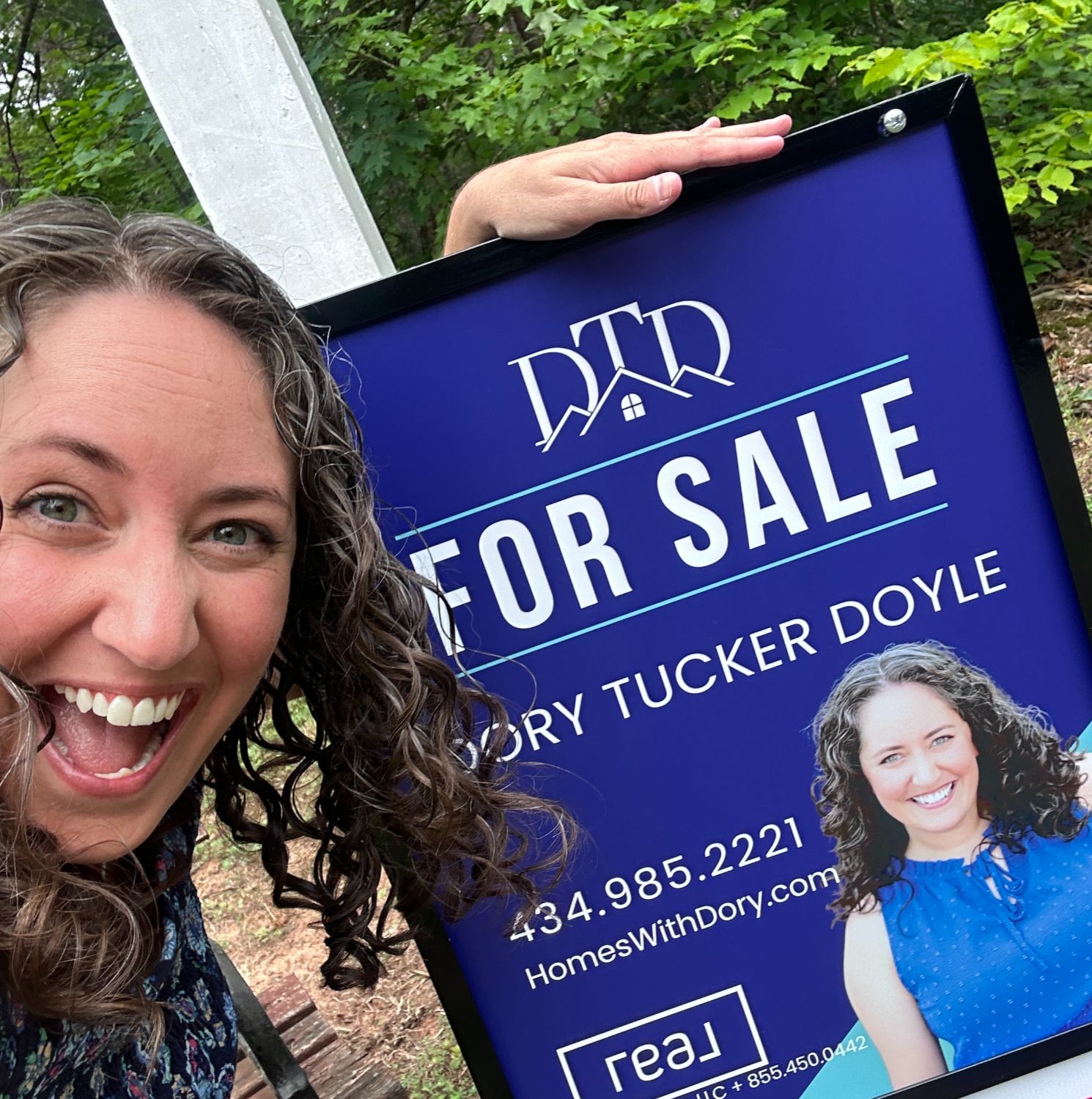 Dory Tucker Doyle with a cheesy grin on her face in front of her real estate sign and open house rider