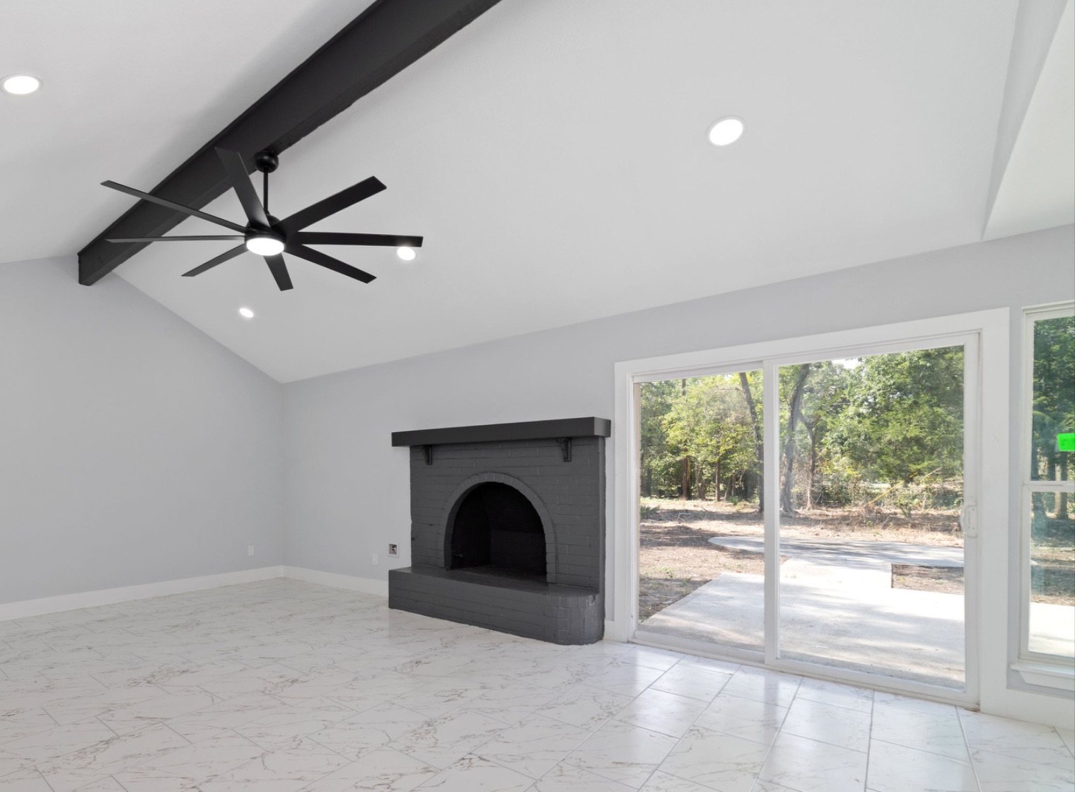 Unfurnished living room with a vaulted ceiling, exposed dark beam, original painted brick fireplace, and sliding glass doors to the patio.