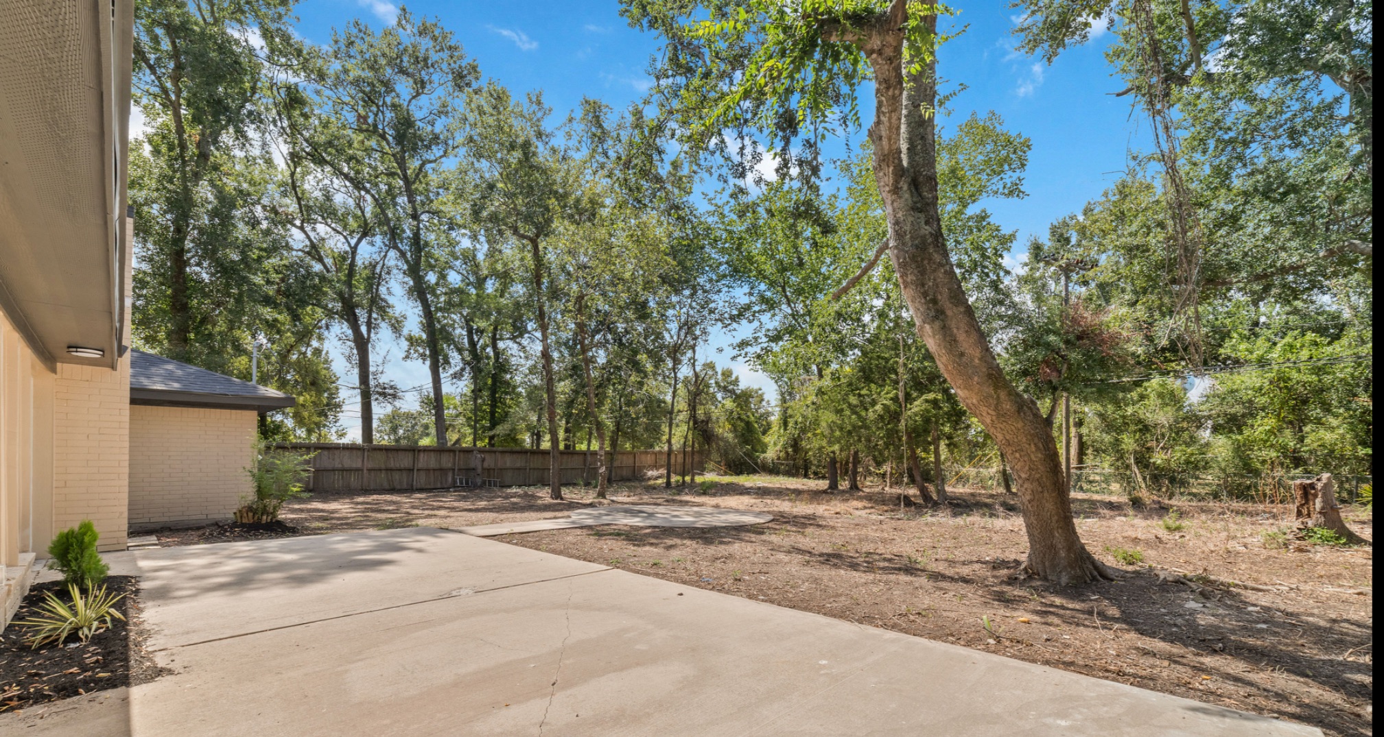 Extended concrete patio behind the home with mature trees and open backyard space.