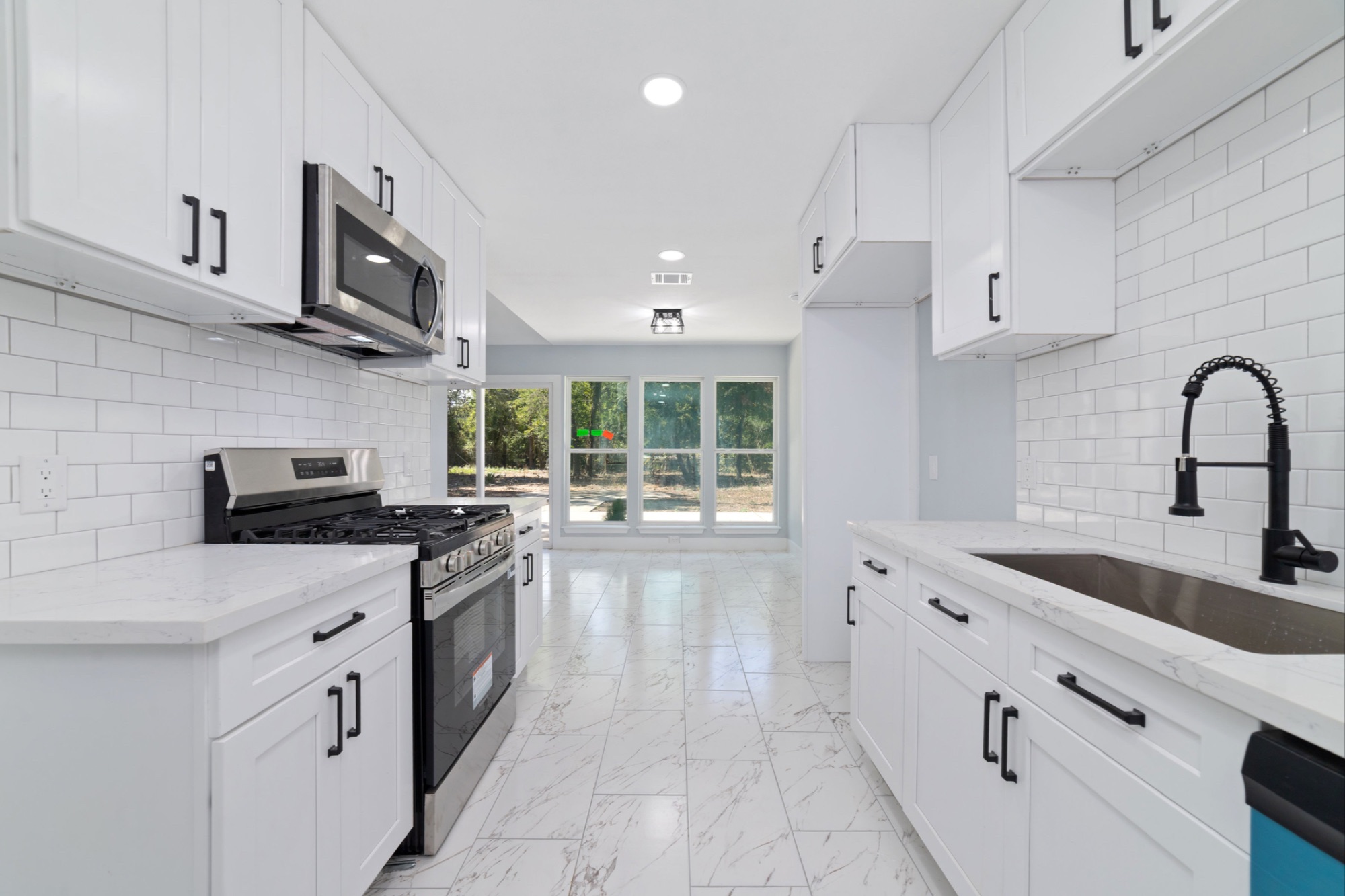 Remodeled galley kitchen with white cabinets, dark hardware, quartz counters, stainless steel appliances, and a view toward the dining area.