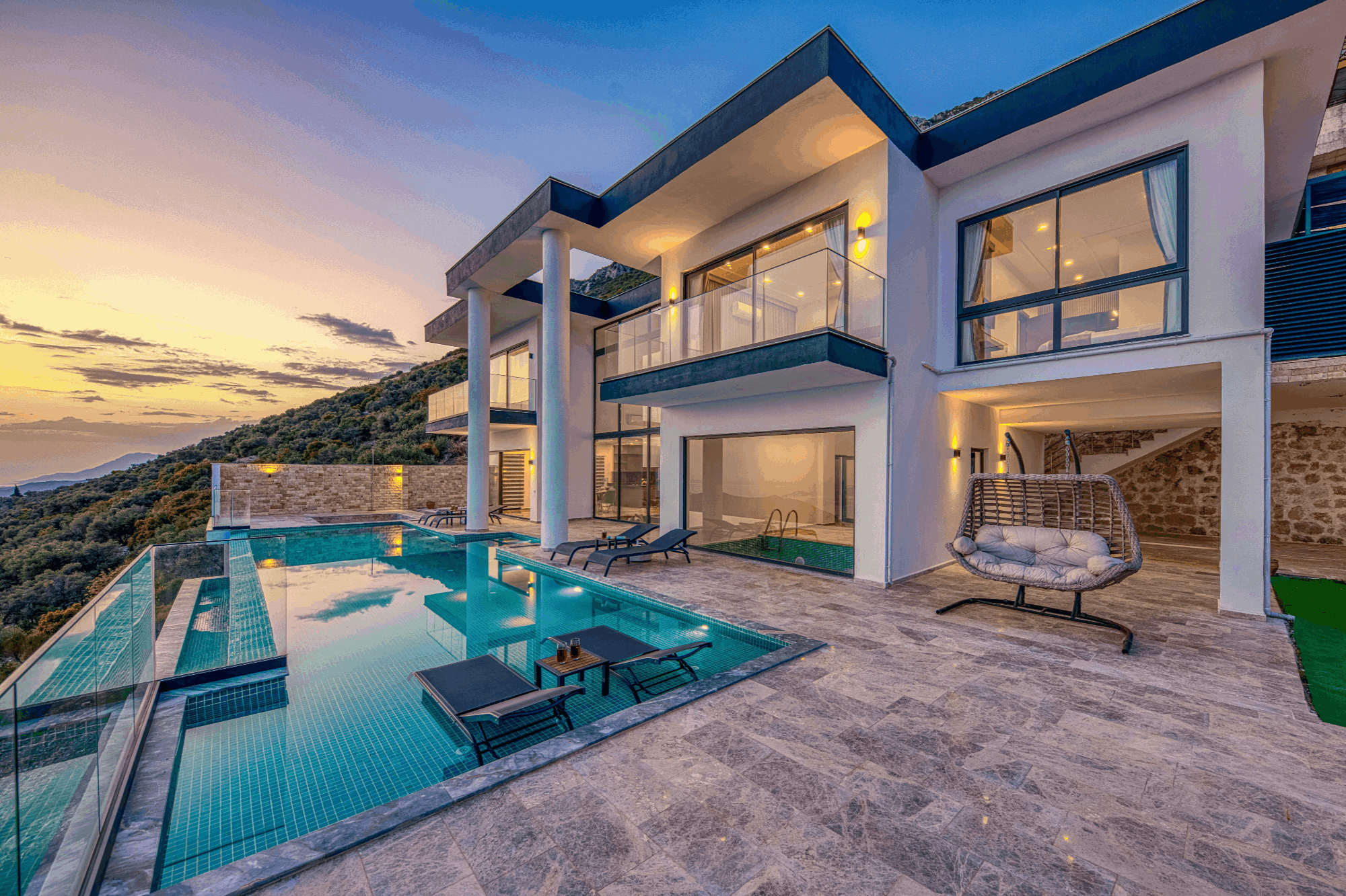 Contemporary home with large windows overlooking a wooded hillside at sunset