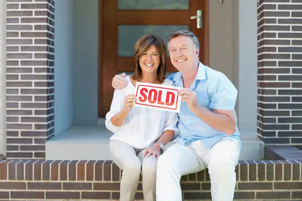 Smiling couple holding a Sold sign in front of their New Jersey home