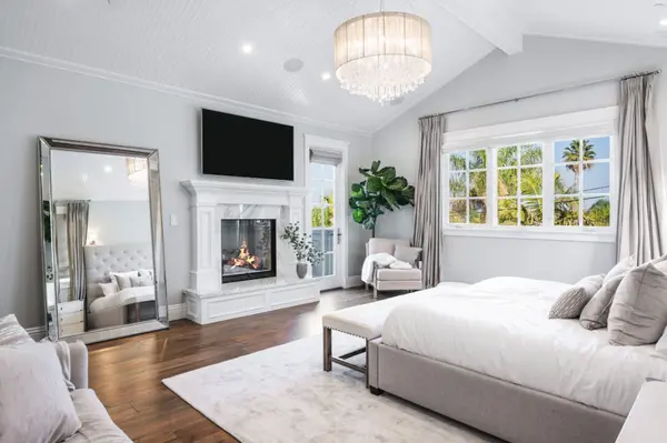 Gorgeous primary bedroom with fireplace, hardwood floors, balcony, and chandelier.