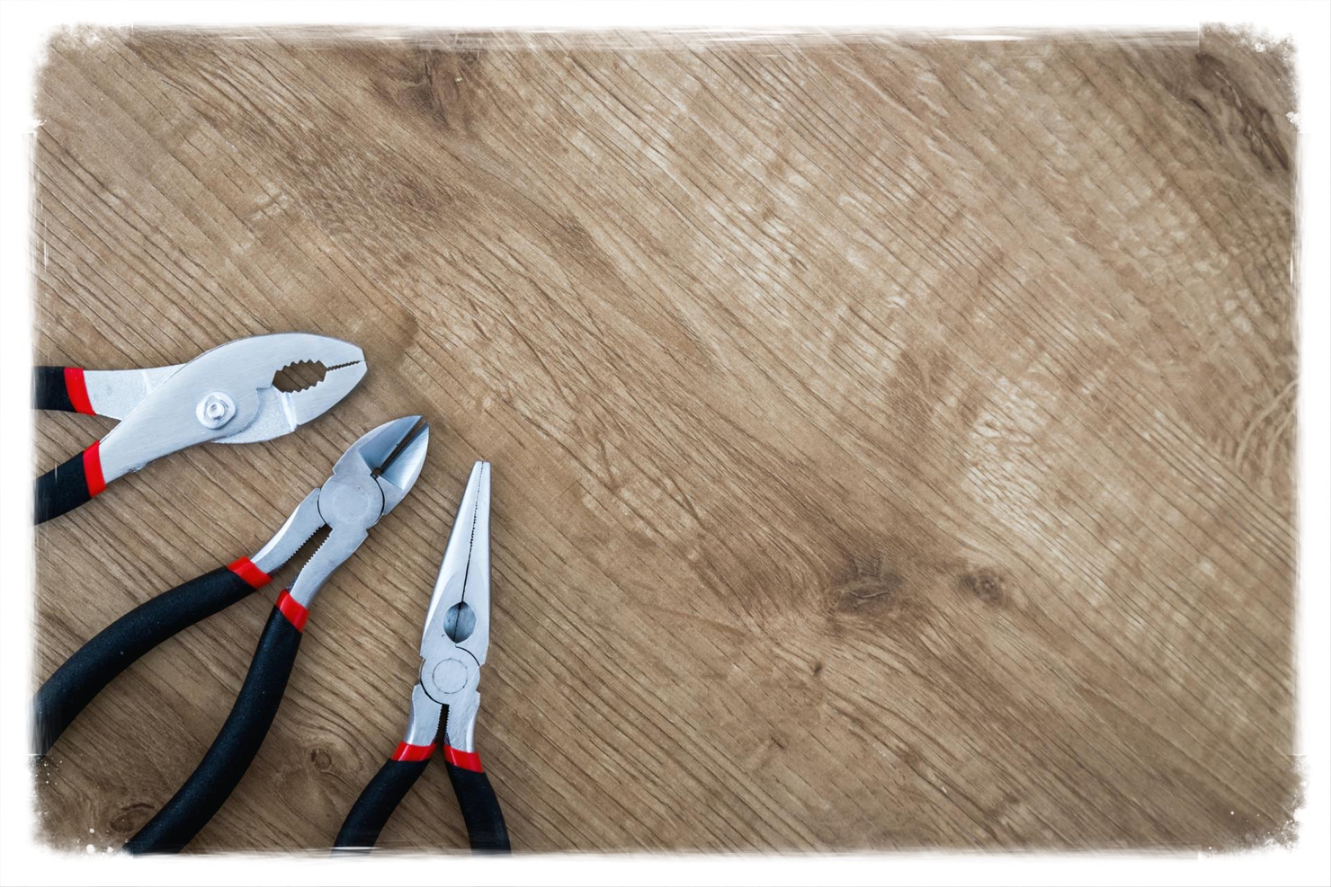 A set of hand tools including pliers arranged on a textured wooden surface, shown in a landscape composition with about a 1.62:1 aspect ratio.