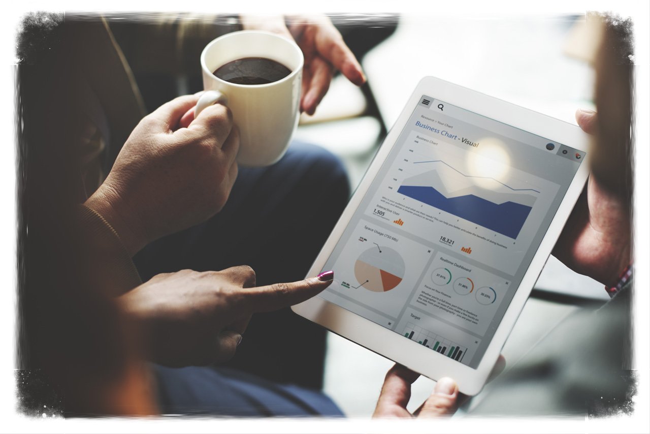 A close-up business scene with hands holding a coffee cup beside a tablet displaying marketing analytics charts and graphs, in a rectangular landscape composition with about a 1.62:1 aspect ratio.