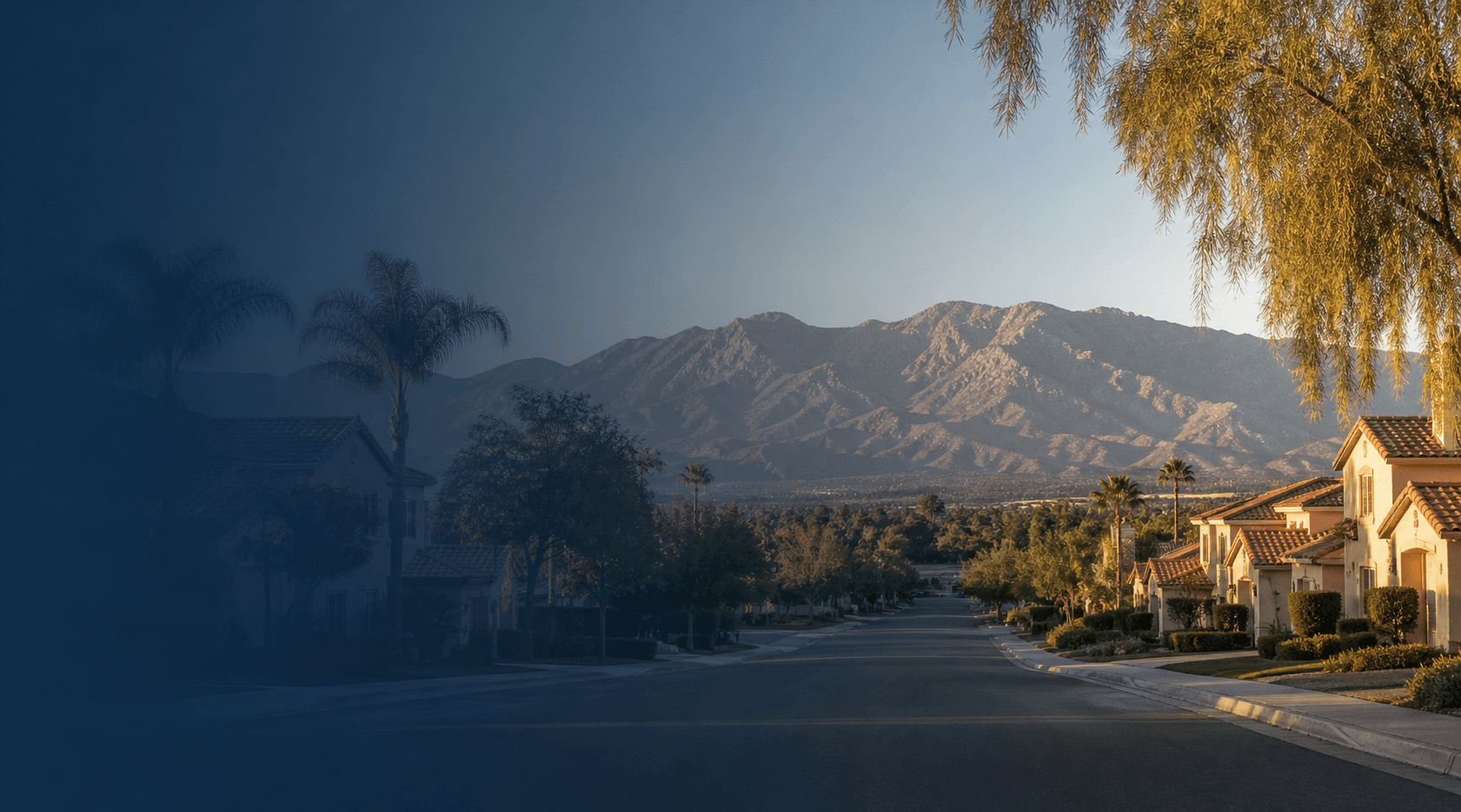 Quiet Inland Empire suburban street with stucco tile-roof homes, palm trees, and the San Bernardino mountains on the horizon