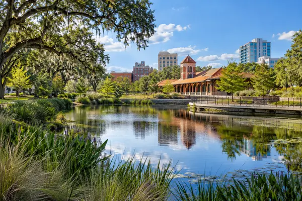 Gainesville-inspired downtown park with a pond, brick depot architecture, live oaks, and a low-rise skyline.