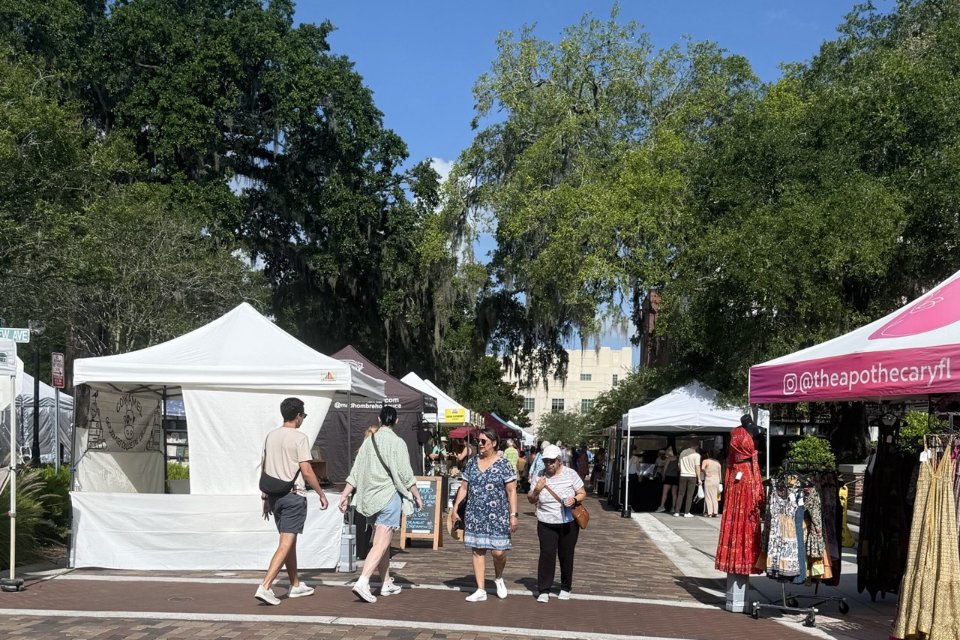 Shoppers walking past vendor tents on the brick street at the Winter Garden Farmers Market in downtown Winter Garden, Florida