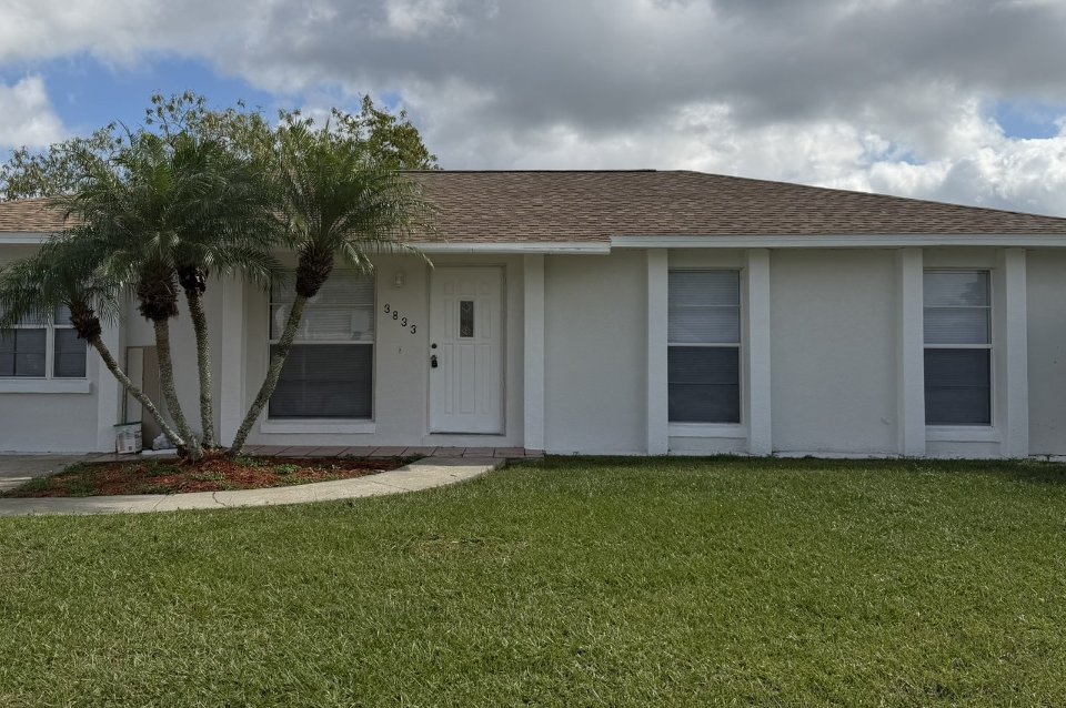 One-story white stucco home with a shingle roof, white front door and palm in Central Florida