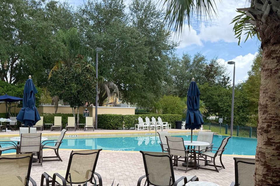 Empty community pool deck with lounge chairs and umbrellas surrounded by palms and oak trees in Central Florida