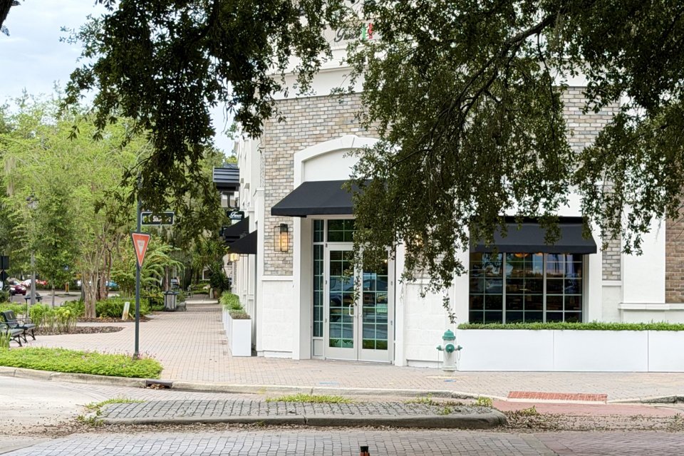 A brick paved corner with a white storefront shaded by live oaks in downtown Windermere, Florida